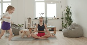 Mother meditating with daughter while active energetic child son playing, calm young mom doing yoga exercise at home for stress relief relaxing with naughty little kid. 4k video footage slow motion