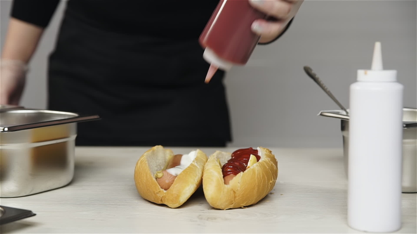 Chef hands in gloves cooks a hot dog, sausage in the dough.