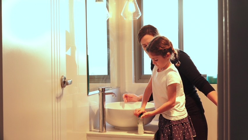 Mother showing her young daughter (age 6) in self isolation how to wash hands properly in home bathroom.