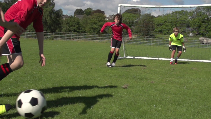 Boys / Children playing soccer / football outdoors on a sunny day. One child kicking the ball past the young goalkeeper and scoring a goal. Slow motion. Stock Video Clip Footage
