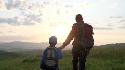 Happy family outdoors trip. Father and son traveling. Little boy child hiker tourist traveler backpacks walking on sunset mountain, hiking vacation travel tourism adventure summer nature. 4 K slow-mo