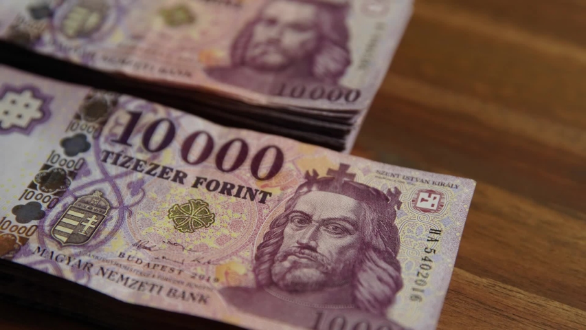 two piles of HUF 10000 Hungarian banknotes on a brown wooden board. (Hungarian forint) Portrait of King St. Stephen. Shallow depth of field, focus on money. Europe Hungary.