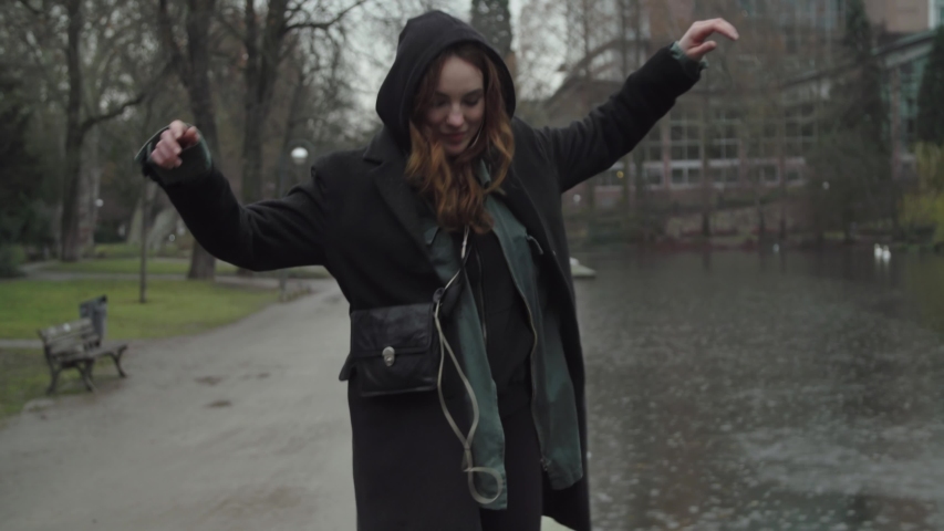 Young woman wearing winter coat laughing and dancing in public park. 