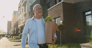Caucasian old man in glasses walking the street home after shopping and carrying packet with grocery. Male senior retired pensioner holding and carrying food in bag outdoors. Coming back from market. - Powered by Shutterstock - Get 15% off with code: PIKWIZARD15
