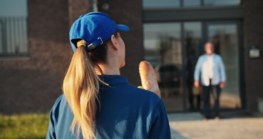 Rear of Caucasian young woman from delivery service in hat bringing packet with food to old man in glasses and giving it outdoors. Back view on female courier giving grocery deliver to grandfather. Royalty-Free Stock Footage #1050466045