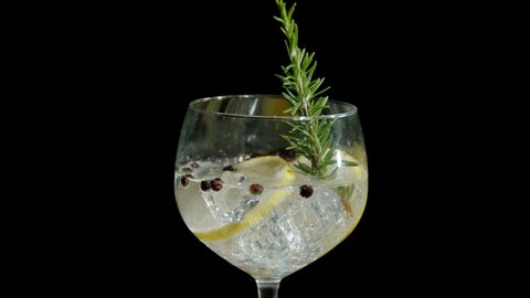 Rosemary falling into a fresh gin and tonic on an isolated black background in super slow motion