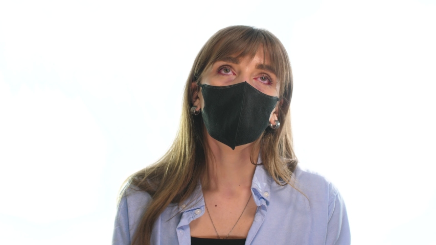 on a white background, a girl with red sore eyes pulls off a black mask from her face to ease her breathing, and red inflammatory processes are visible around her mouth Royalty-Free Stock Footage #1050471007