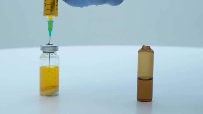 Closeup shot of doctor hands preparing vaccine solution for injection. scientist in blue gloves mixing yellow liquid with sediment in glass phial. Medicine, healthcare concept, clinic vaccination | Shutterstock HD Video #1050493561