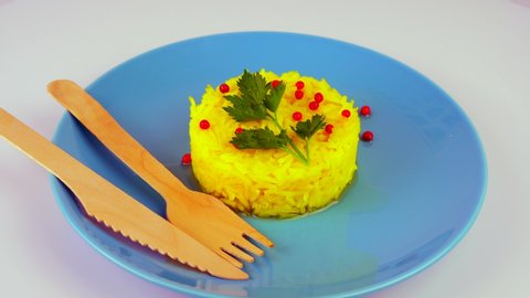 yellow vegetarian rice dish n atale with a touch of red pepper and green leaf, simplicity of the dish, on a plate with organic wooden forks and a knife. 4k25ftp