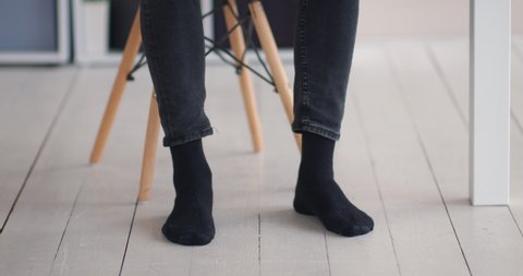 Working at home comfortably. Man in socks stepping rhythm at workplace under table, close up