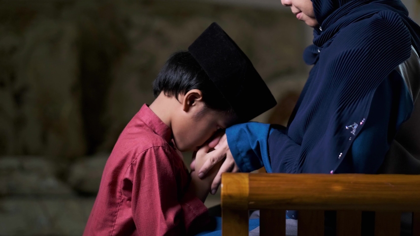 A malay boy in malay traditional costume kiss his mother's hand and ask for forgiveness during Hari Raya festive | Shutterstock HD Video #1050508054