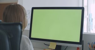 Young women work on computer with green mock-up screen. Girl in cozy clothes sitting in living room using laptop. Over shoulder camera shot. 4k video footage slow motion