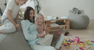 Happy mom and cute kids having fun talking using laptop at home, smiling mother teach little children online shopping. Young woman works from home. Self-isolation. 4k video footage slow motion