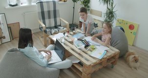 Happy mom and cute kids sitting at home, mother talking with little children drawing and playing with toys . Young woman works from home. Self-isolation. 4k video footage slow motion
