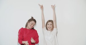 Two smiling crazy girl in summer clothes having fun. Young women dancing . Models posing on white wall background. Female showing positive face emotions. 4k video footage slow motion