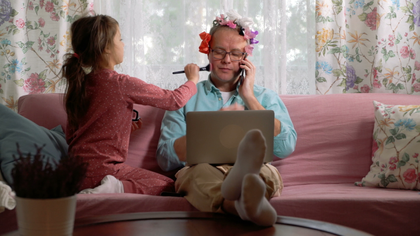 Home quarantine self-isolation. A middle-aged man working remotely from home. His little daughter getting in the way all the time and trying to make up his face | Shutterstock HD Video #1050516274