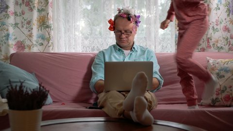 Home quarantine self-isolation. A middle-aged man working remotely from home. His little daughter getting in the way all the time. She tieing bows on his head