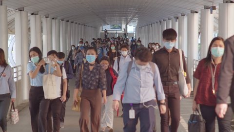 Bangkok, Thailand - Apr 7, 2020: Crowded Asian people wear face mask walking in pedestrian walkway. Coronavirus disease Covid-19 pandemic outbreak, city life, or air pollution concept. 4K slow motion