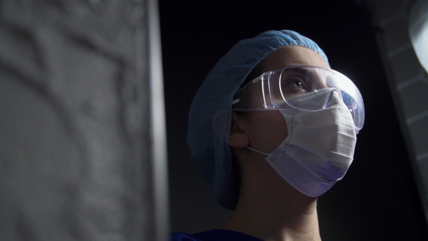 health, medicine and pandemic concept - tired young female doctor or nurse in hat and face protective mask taking goggles off over black background Royalty-Free Stock Footage #1050532531
