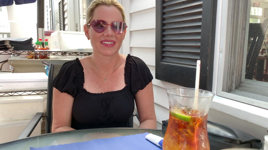 a beautiful woman in heart shaped glasses takes a drink from her cocktail at a restaurant