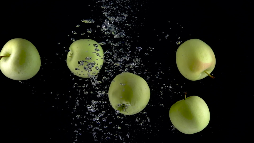 Apples fall in water on black background. Slow motion 250fps