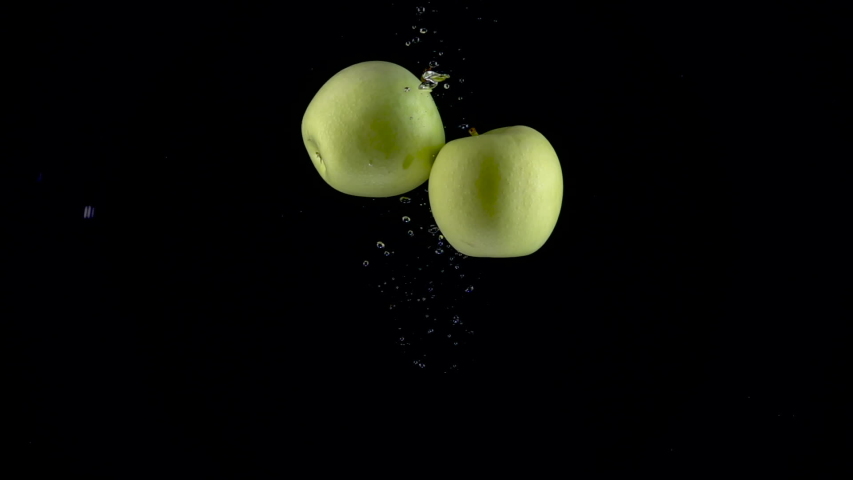 Apples fall in water on black background. Slow motion 250fps