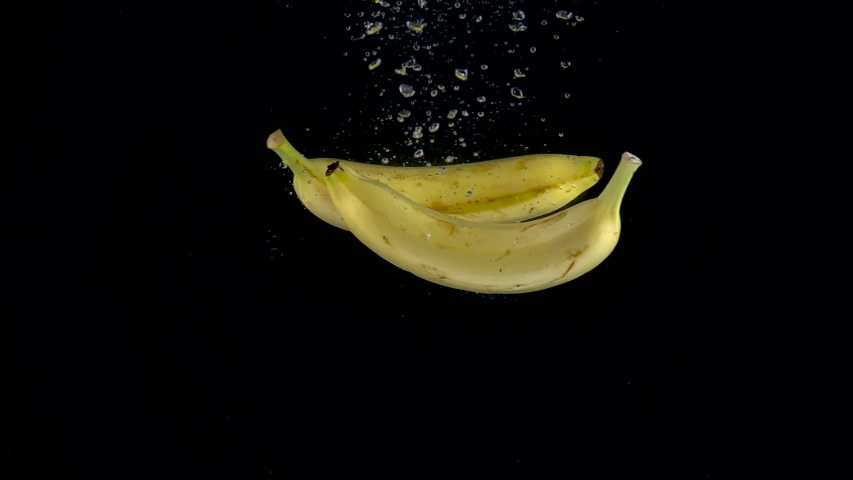 Bananas fall into the water on a black background. Slow motion 250fps