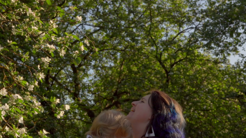 Mom is throwing up and kissing a little adorable daughter in white dress in the apple tree garden
