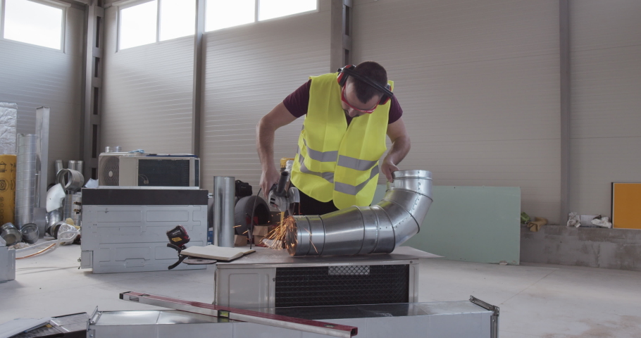 A construction worker cuts a metal with an angular grinder. 