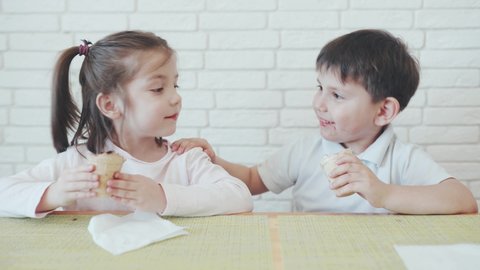 Funny kids. A Caucasian boy and girl eat chocolate ice cream. The boy touches the girl's nose with ice cream. Brick wall is on the background. Kids having fun. Children in self-isolation. Quarantine.