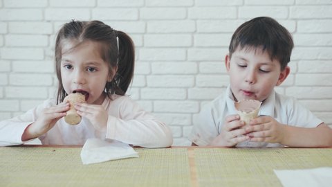 Funny kids. A Caucasian boy and girl with dark hair eating chocolate ice cream. Children share ice cream. Brick wall is on the background. Kids having fun. Children in self-isolation. Quarantine.