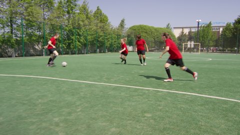 Team of young female players running on green field, dribbling soccer ball and scoring a goal into goal of opponent while training outdoors on sunny summer day: film stockowy