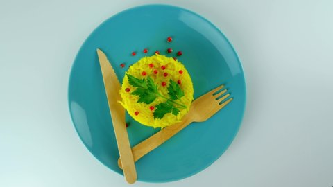 yellow vegetarian rice dish n atale with a touch of red pepper and green leaf, simplicity of the dish, on a plate with organic wooden forks and a knife. Top view food. 4k25ftp