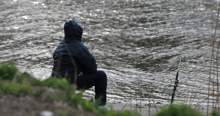 Rear view unrecognizable fisher catch a fish sitting near river