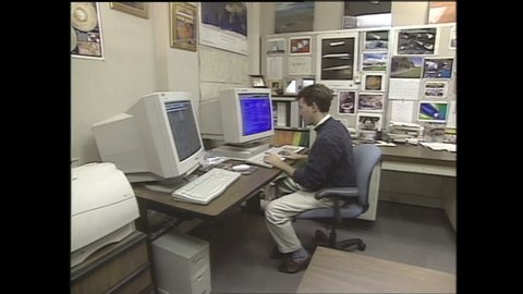 1990s: Man sits in front of computer in office. Man typing on computer. Man looks at monitor.