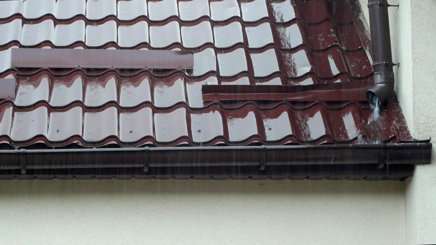 Heavy rain falls on the roof, covered with corrugated brown metal. Water from the downpipe runs down the gutter Royalty-Free Stock Footage #1050565651