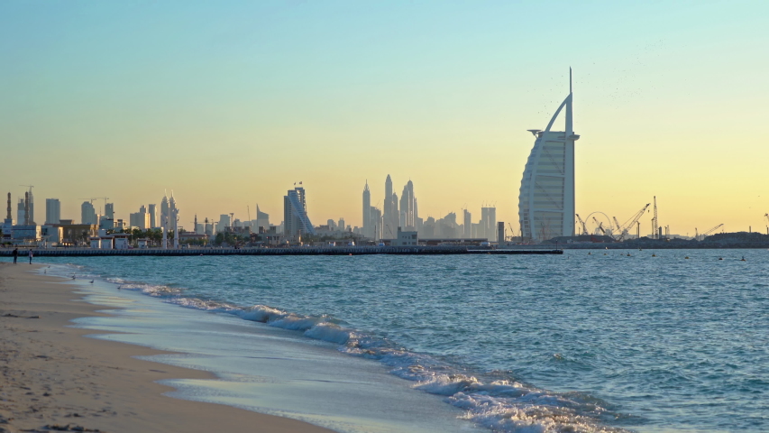 Dubai Downtown skyline with waves on sea beach, United Arab Emirates or UAE. Financial district in urban city. Skyscrapers at sunset.