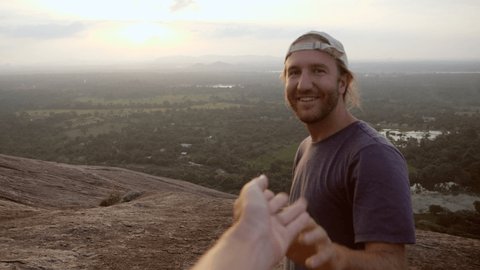 Couple holding hands man leading girlfriend on top of rock at sunset overlooking Sigiriya and green lush tropical jungle in Sri Lanka - Follow me to concept 