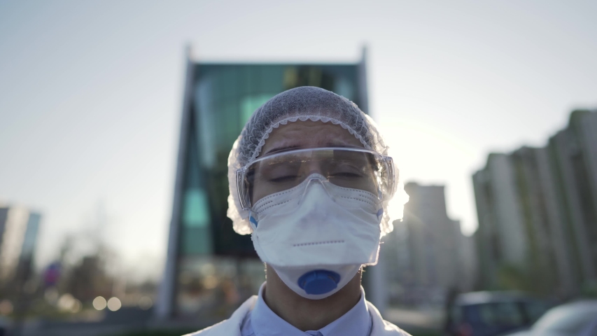 Coronavirus doctor standing in front of modern clinic building,working in the isolation ward.Medical professional in protective equipment in fight against COVID-19.Triage performing medical worker. | Shutterstock HD Video #1050583300