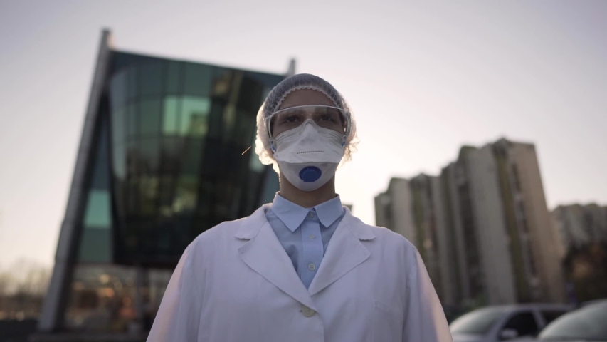 Coronavirus doctor standing in front of modern clinic building,working in the isolation ward.Medical professional in protective equipment in fight against COVID-19.Triage performing medical worker. | Shutterstock HD Video #1050583369