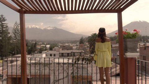 Beautiful Misti Mountain, with Arequipa city town buildings in foreground. Girl watching on balcony. DRONE aerial view. View of snow capped mountains in background at sunset. Shot in Peru.