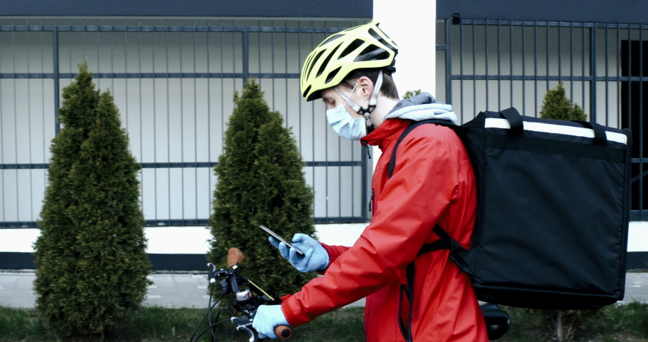 Courier wearing medical mask checking customer address on his phone, food delivery during virus outbreak. Coronavirus, COVID-19, safe delivery Royalty-Free Stock Footage #1050598978