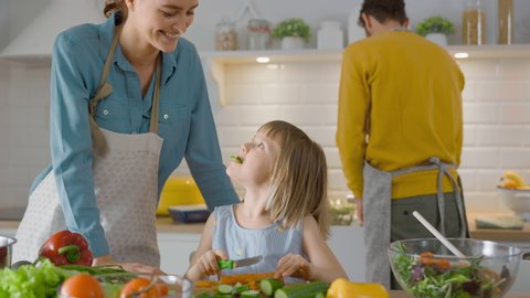 In the Kitchen: Mother and Cute Little Daughter Cooking Together Healthy Dinner. Mom Teaches Little Girl Healthy Habits and how to Cut Vegetables for the Salad. Cute Child Helping Her Caring Parents