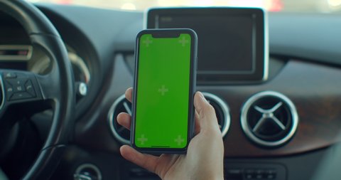 Lviv, Ukraine - April 4, 2020: Man hand using chromakey mobile phone with empty green screen in modern car. Mockup touchscreen. internet searching.