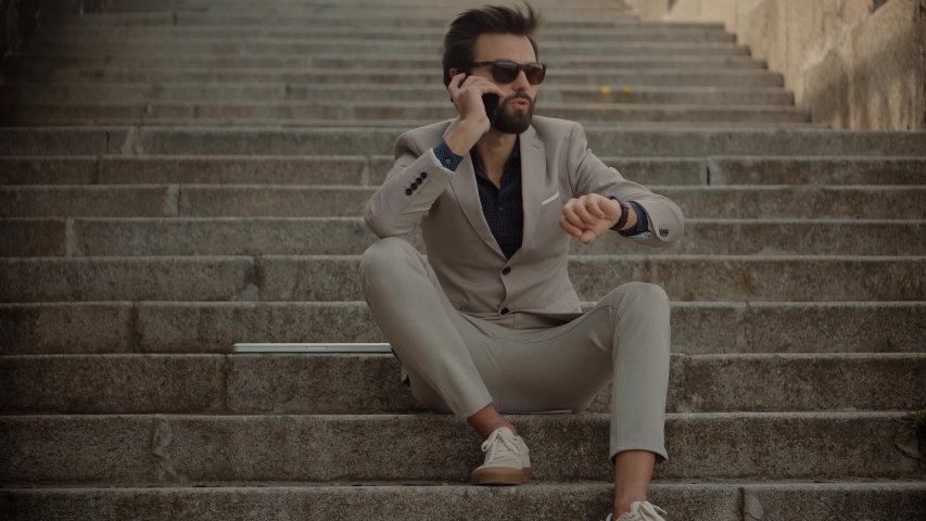 Businessman Sitting on Stairs And Talking On Mobile Phone.Freelancer Internet Online Meeting Webinar And Calling.Man Freelance With Smartphone Outdoors.Businessman With Phone On Steps Remote Working. | Shutterstock HD Video #1050611329