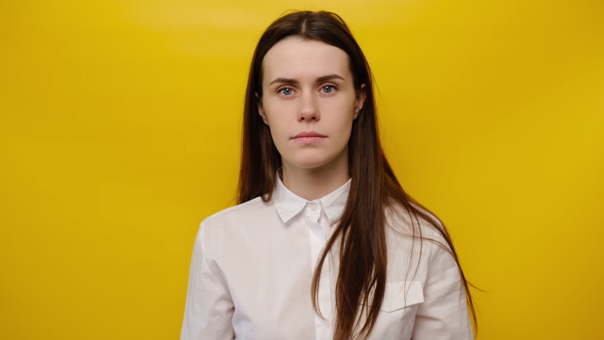 Scared young woman isolated on yellow studio background peep through fingers feel frightened terrified, stares with widely opened eyes, wears white shirt, hides face from someone, copy space aside Royalty-Free Stock Footage #1050611599