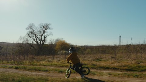 Little boy flies over the wheel of a runbike while riding in nature. Hard fall, son learns to ride a bike, slow-motion video