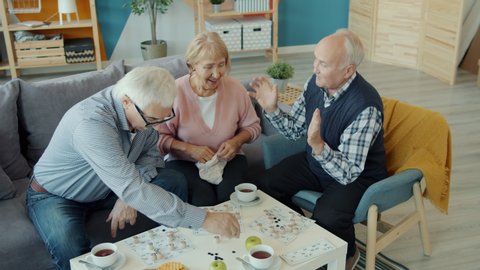 Old men and woman friends are playing lotto doing high-five showing thumbs-up in house. Board games, indoor entertainment and lifestyle concept.