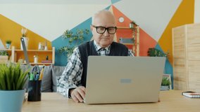 Slow motion of cheerful old man making online video call with laptop at home talking gesturing looking at computer screen. People and communication concept.