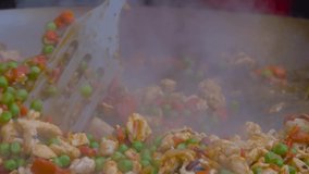 Outdoor cooking, cookery, gastronomy and street food concept. Super slow motion: chef cooking fried chicken meat pieces, peppers, peas in huge wok at summer food market - close up view - Powered by Shutterstock - Get 15% off with code: PIKWIZARD15